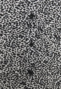 Schwarz-weißer Leopardenmuster-Stoff mit glatter Textur und schwarzem Knopfverschluss. Geflecktes Muster in unterschiedlichen Formen und Größen.