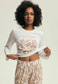 Biała koszula z długim rękawem z roślinnym wzorem w delikatnym beżu, w zestawie z pasującymi spodniami piżamowymi z liściastym wzorem i elastycznym pasem.
