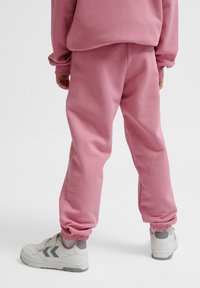 Fleece joggers in een zachte roze kleur met geribbelde boorden en een elastische tailleband. Gecombineerd met witte sneakers met grijze accenten.