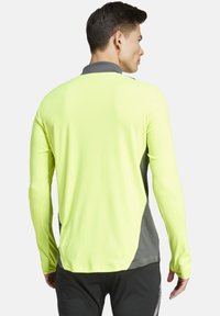 Maglietta atletica a maniche lunghe di un vivido giallo neon con dettagli grigi, caratterizzata da una texture del tessuto liscia e un design aderente.