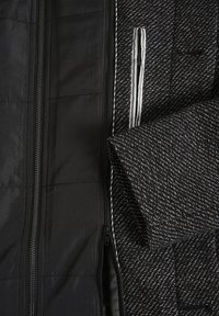 Wnętrze czarnej pikowanej kurtki z teksturowanym szarym i czarnym wzorem jodełki, z paskowanym wewnętrznym kieszonką i kontrastowym zamkiem.