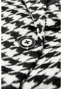 Tissu à motif pied-de-poule noir et blanc avec une texture douce, orné d'un bouton rond noir à quatre trous.