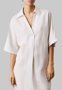 Witte, kortaf met mouwen, gecollarde jurk met een V-hals. Gemaakt van een gladde, lichte stof met een ontspannen pasvorm en een minimalistisch ontwerp.