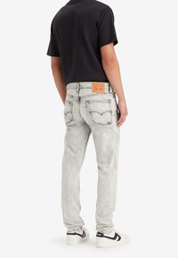 Ljusgrå denimjeans med tapered fit, med en lädermärke patch, femfickorsdesign och subtila slitningar.