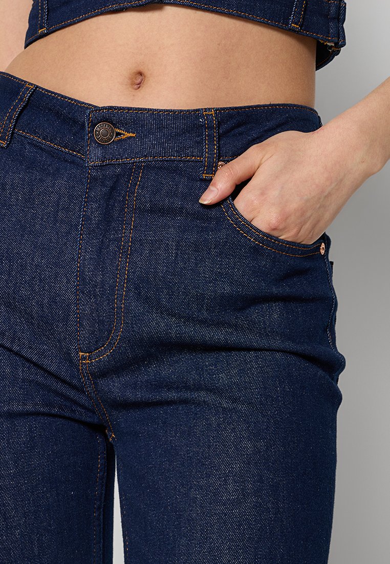 Granatowe dżinsy z pomarańczowym haftem, z przednią kieszenią i zapięciem na guzik. Gładka faktura i dopasowany krój.