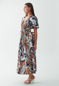 Robe maxi avec un décolleté en V profond, une taille cintrée et des manches courtes évasées. Présente un motif floral en teal, orange et marine. Tissu semblable à de la soie.