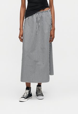 Γυναίκα που φοράει μαύρο τοπ με ρυτιδώσεις, μαύρη και λευκή midi φούστα καρό και μαύρα sneakers ψηλά με λευκά κορδόνια.