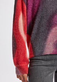 Pull en tricot multicolore présentant des nuances de rouge, de rose et de gris, avec une texture douce, des poignets côtelés et une coupe décontractée.