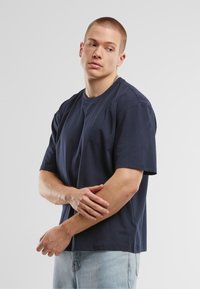 T-shirt din bumbac de culoare bleu închis, cu mâneci scurte și guler rotund, purtat cu blugi de denim de culoare bleu deschis. Design simplu și lejer.