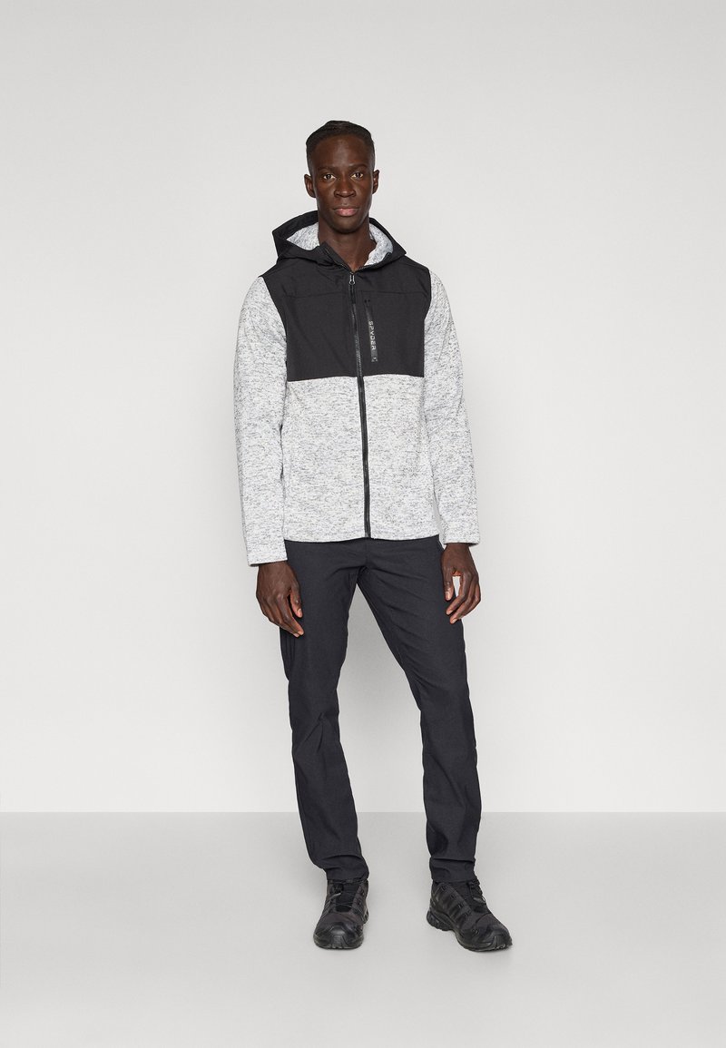 Haut de hoodie zippé gris et noir avec une partie supérieure texturée en tricot et une partie inférieure lisse. Associé à un pantalon noir et des chaussures de sport noires.