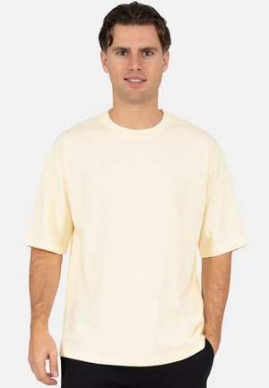Light yellow cotton t-shirt with short sleeves, round neckline, relaxed fit, and soft texture. Minimal detailing, held in casual pose.