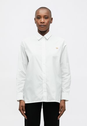 White long-sleeve shirt with a collar, featuring a small embroidered gold animal design on the chest and a button-down front.