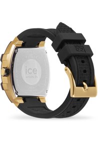 Reloj con correa de goma negra y caja en tono dorado, con parte trasera de acero inoxidable y acentos texturizados. Cuenta con un cierre de botón a presión para un ajuste seguro.
