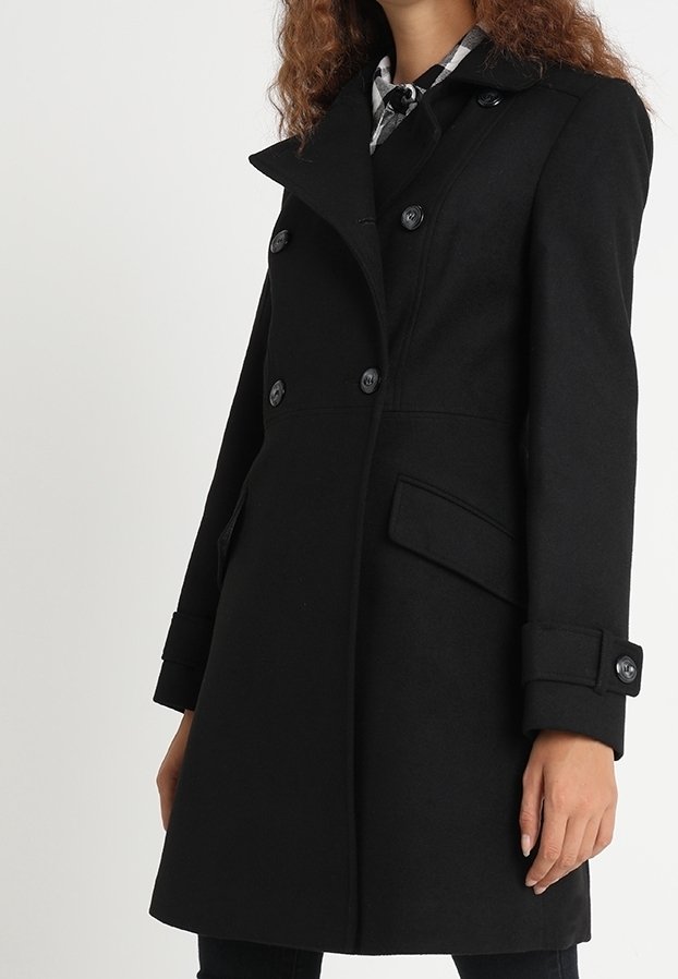 Svart dubbelknäppt kappa med klyvkrage, sidofickor och knappdekorationer. Tillverkad av ett strukturerat tyg.