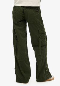 Pantalons cargo verts avec taille élastique, plusieurs poches latérales et zippers au niveau des chevilles. Fabriqués en tissu léger, ils offrent une coupe décontractée.