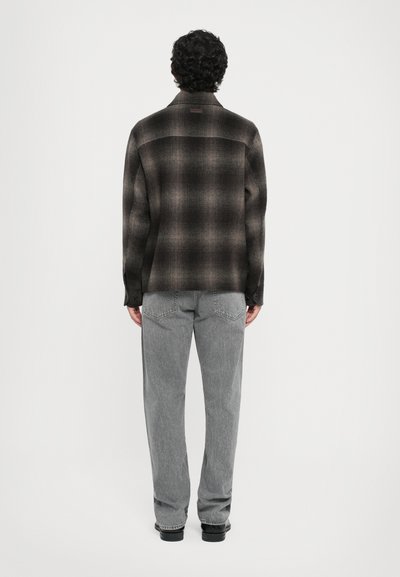 Black and gray plaid shirt with a button-down collar, long sleeves, and a straight cut. Worn with light gray pants and black shoes.