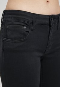 Mustat farkut, joissa on keski-nouseva vyötärö, viisi taskua ja huomaamatonta ommelta. Liu'utettu pinta ja kestävä kangas, jossa on nylkydentukkakuva.