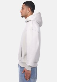 Hellgrau Hoodie mit Kängurutasche, gerippten Bündchen und Kapuze. Weicher, strukturierter Stoff, einfaches Design und minimale Markenkennzeichnung auf der Vorderseite.