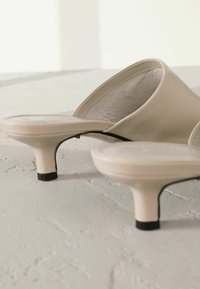 Beige-nahkakengät, joissa on pyöreä kärki, matala korko ja teksturoitu pohja. Mustat kumit upsit kantapään perustassa. Sileät viimeistellyt pinnat.