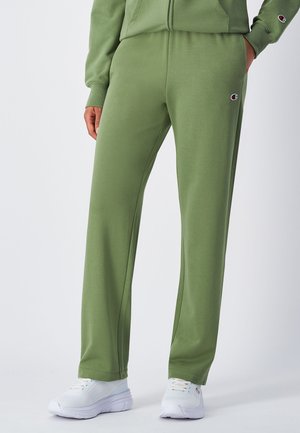 Pantalons de survêtement verts, élastiques, avec une coupe décontractée, dotés de poches latérales et d'un petit logo sur la hanche, associés à des baskets blanches.