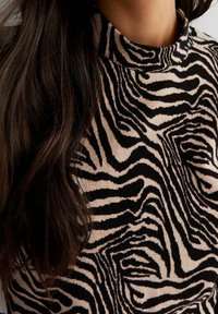 Svart och tan zebra-randig polokrage-tröja med en mjuk textur och figurnära design, vilket visar tygmönstret och detaljerna vid halsringningen.