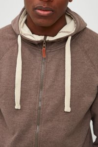 Sudadera con cremallera marrón, con cordones color crema y un forro interior en contraste. Presenta una cremallera en el frente y está hecha de un tejido suave y texturizado.