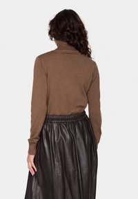 Brauner Rollkragenpullover aus Strickstoff, kombiniert mit einem schwarzen Lederrock mit elastischem Bund. Die Rückansicht hebt die Texturen hervor.