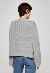 Grå kabelstickad tröja med rund halsringning, sänkta axlar och ribbade muddarna. Har en kortare längd och ett texturerat mönster över hela.