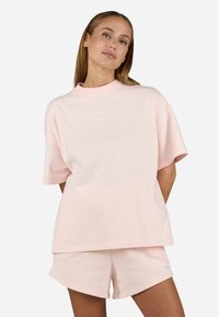 Lys rosa matchende sett som inkluderer en løs t-skjorte med kort erm og rund hals, i kombinasjon med matchende shorts, begge i mykt stoff.