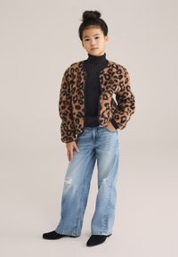 Giacca in pelliccia sintetica maculata in marrone e nero, dolcevita nera a costine, jeans a gamba larga celeste chiaro con effetto usato e stivali neri alla caviglia.