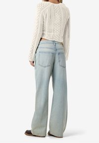 Stickad krämfärgad tröja med ett strukturerat mönster, tillsammans med högmidjade ljusblå vida jeans. Anmärkningsvärda detaljer inkluderar bakfickor och en avslappnad passform.