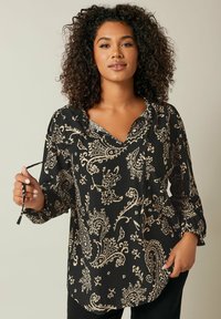 Blusa nera con motivo paisley beige, scollo a V, maniche lunghe e tessuto testurizzato. Il modello tiene un dettaglio con cravatta al colletto.