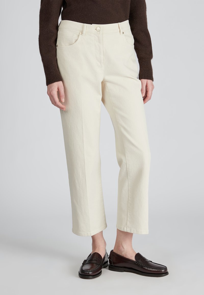 Pantaloni bianchi tagliati realizzati in tessuto testurizzato, con tasche anteriori e chiusura con bottone. Abbinati a mocassini marroni scuri.