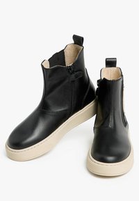 Bottines en cuir noir avec une fermeture éclair, semelles en caoutchouc crème et une texture lisse. Équipées d'une languette pour un enfilage facile.