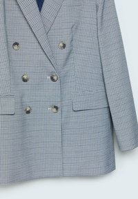 Ruudullinen sinivalkoinen kaksirivinen bleiseri metallinapeilla, sakaraharteilla ja etutaskuilla. Teksturoitu kangas.