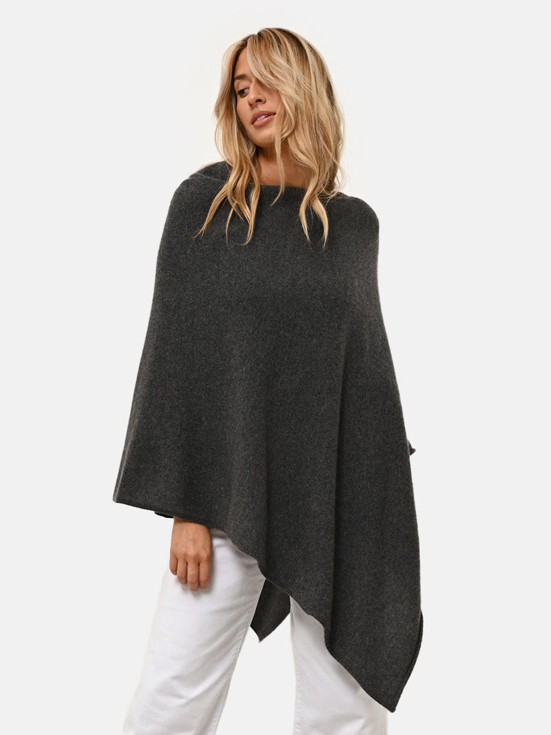 Poncho gris oscuro, mezcla de lana, forma rectangular con dobladillo asimétrico, textura suave, diseño superpuesto, usado sobre pantalones blancos.