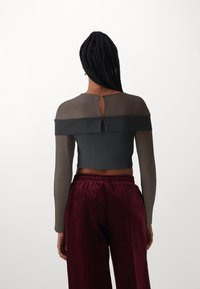 Grauer Cropped-Top mit transparenten Ärmeln und einem Schlüsselloch-Rücken, kombiniert mit bordeauxroten Samthosen mit elastischem Bund und seitlichen Nähten.