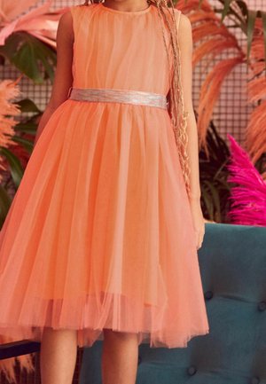 Robe en tulle pêche avec design sans manches, corsage froncé et ceinture argentée. Texture douce et superposée avec une jupe mi-longue.