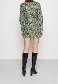 Robe courte à fleurs avec manches longues bouffantes, présentant un fond noir orné de fleurs multicolores. Portée avec des bottes noires à talons montant jusqu'aux genoux.