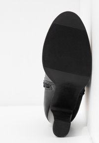 Suela de zapato de cuero negro con un agarre texturizado. Forma redondeada, diseño sencillo y un ligero tacón. Sin marcas ni adornos visibles.