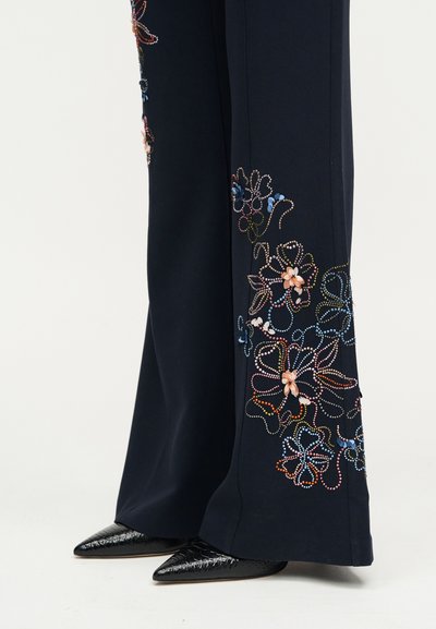 Μαριν μπλε φαρδιά παντελόνια με πολύχρωμη κεντημένη λουλουδάτη διακόσμηση με χάντρες κοντά στο τελείωμα, σε συνδυασμό με μυτερές μαύρες υφασμάτινες δερμάτινες παπούτσια.