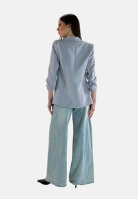 Blazer grigio chiaro su misura con spalle strutturate, abbinato a jeans larghi blu chiaro. Tacchi neri appuntiti completano l'outfit.
