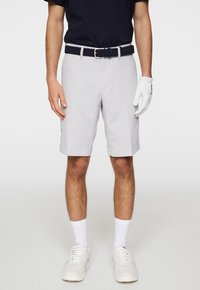 Ljusgrå shorts med en slät textur, prydda med ett bälte med vävd design, som bärs med en marinblå skjorta och vita träningsskor.