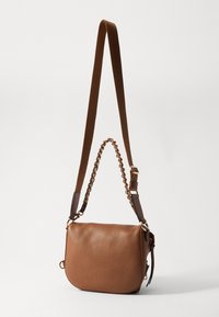 Hnědá kožená crossbody taška s texturovaným povrchem, zaobleným tvarem a popruhem zdobeným řetězem. Má nastavitelný popruh a boční detail s třásněmi.