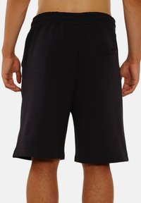 Schwarze Baumwollshorts mit elastischem Bund, knielangem Schnitt und einer hinteren Tasche mit abgerundetem Eingang.