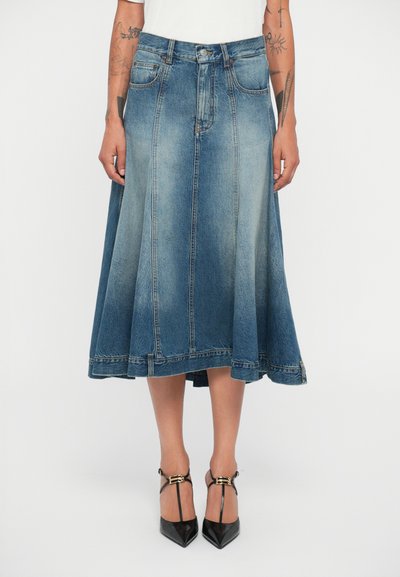 Hellblauem Jeansrock mit ausgestelltem, knielangem Design, sichtbaren Nähten und hohem Bund. Trägt schwarze Riemchen-Absätze.