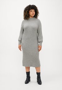 Vestido de malha cinza com gola alta e mangas longas e bufantes, atingindo a metade da panturrilha. Usado com botas pretas até o tornozelo.