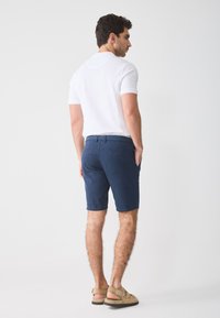 White polo shirt, navy blue shorts with front and back pockets, and tan sandals. Smooth fabric, classic fit, and woven belt detail.