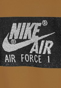 Diseño del logo de Nike Air Force 1 con texto blanco grande sobre un fondo negro, presentando un swoosh, encima de una sección marrón sólida.