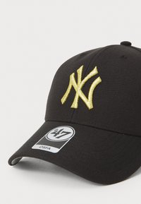 Svart baseballcaps med et hevet gullbrodert "NY"-logo. Inkluderer et merke som angir størrelse som OSFA. Glatt, strukturert stoff med buet skjerm.